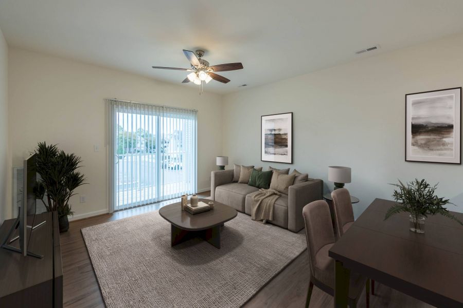 Modern living room with a sofa, coffee table, TV, dining table, and sliding glass doors letting in natural light.