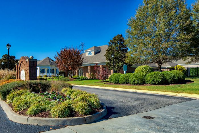Entrance to a residential neighborhood with landscaped greenery, trees, and a brick sign on a sunny day.