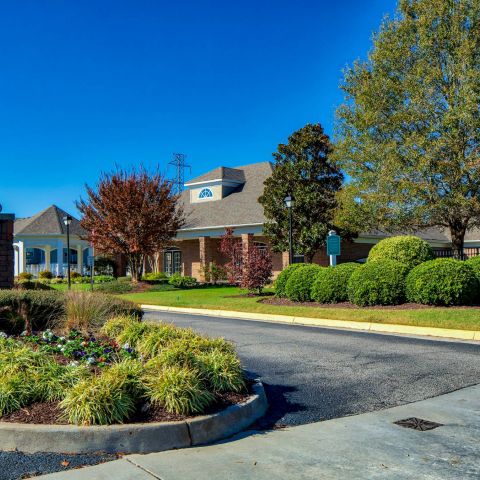 Entrance to a residential neighborhood with landscaped greenery, trees, and a brick sign on a sunny day.
