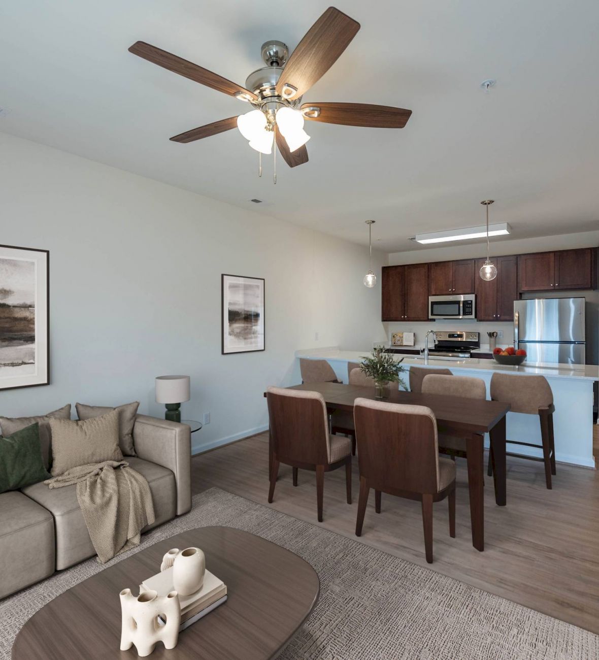 Modern open-concept living and dining area with neutral décor, wood furniture, and a bright kitchen in the background.