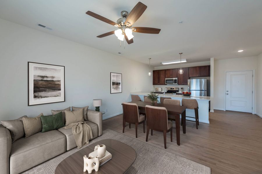 Modern open-concept living and dining area with neutral décor, wood furniture, and a bright kitchen in the background.