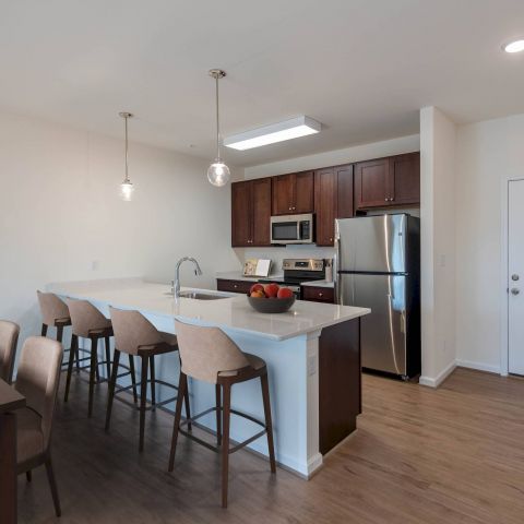 Modern kitchen with island seating, stainless steel appliances, and a dining table on wood flooring.