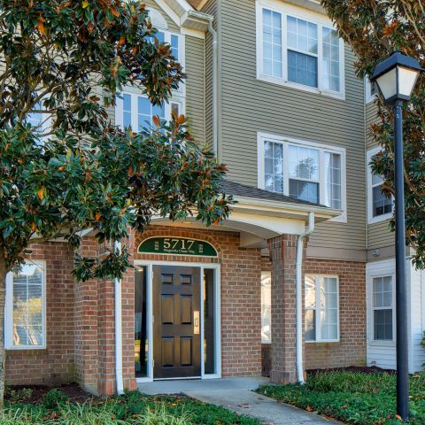 Brick apartment building with tan siding, black door, trees, and a streetlamp in front.