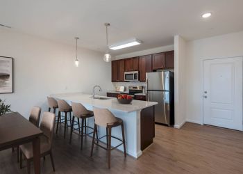 Modern kitchen with island seating, stainless steel appliances, and a dining table on wood flooring.