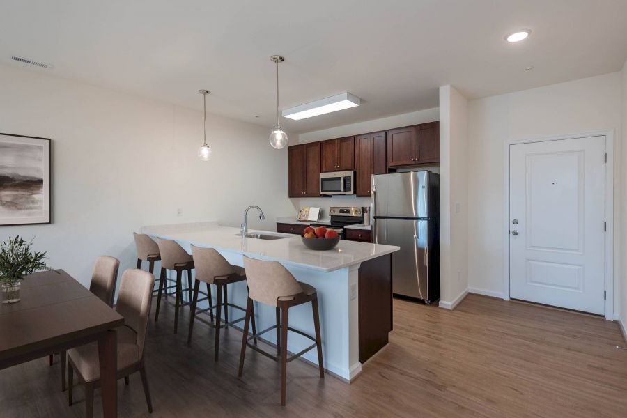 Modern kitchen with island seating, stainless steel appliances, and a dining table on wood flooring.