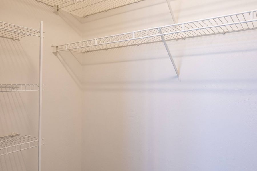 Empty walk-in closet with white wire shelving on the walls and no items stored on the shelves.