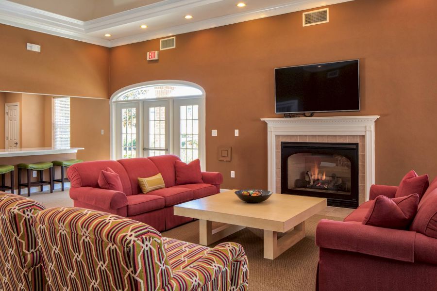 Modern living room with red sofas, patterned chairs, fireplace, TV, and a breakfast bar with green stools.