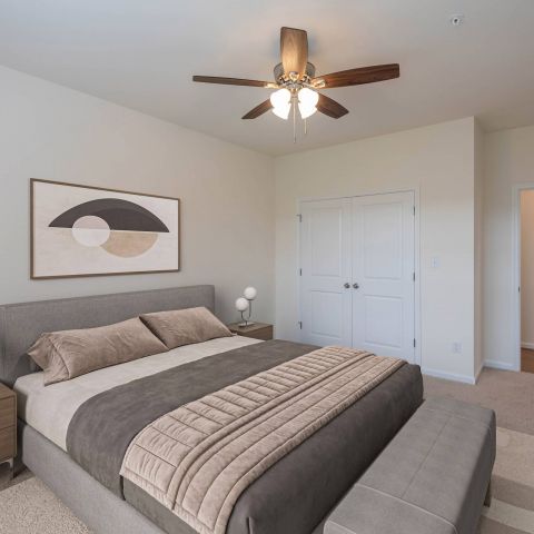 Modern bedroom with a gray bed, two nightstands, abstract art, and a ceiling fan with lights.