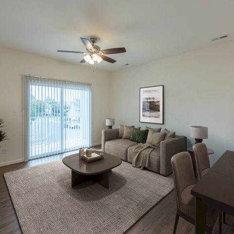 Modern living room with a sofa, coffee table, TV, dining table, and sliding glass doors letting in natural light.